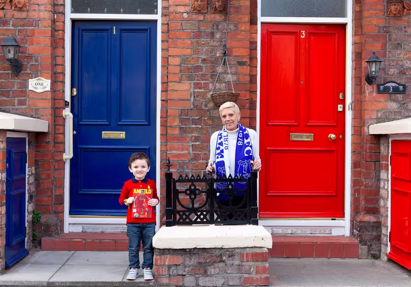A boy and a woman with an Everton scarf in front of a blue and a red front door